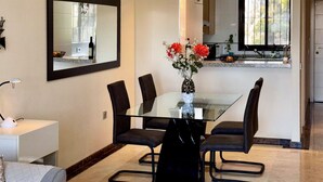 A modern dining area with a glass table surrounded by black chairs, a vase with flowers, and a kitchen in the background. - Awesome apartment in LA CALA DE MIJAS (MIJA (LA CALA DE MIJAS (MIJA)