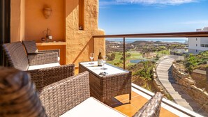 A balcony with wicker furniture, a table with a bottle and glasses, and a view of a golf course and buildings. - Awesome apartment in LA CALA DE MIJAS (MIJA (LA CALA DE MIJAS (MIJA)