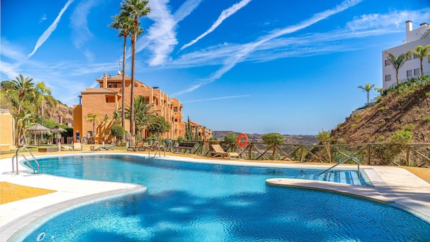 A swimming pool with lounge chairs, palm trees, and a building with multiple balconies. - Awesome apartment in LA CALA DE MIJAS (MIJA (LA CALA DE MIJAS (MIJA)
