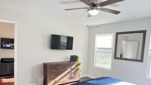 A bedroom with a bed, a ceiling fan, a TV, a dresser, and a window.