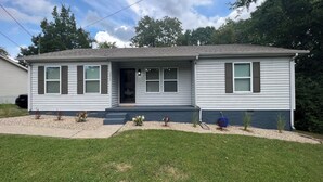A single-story house with a front porch, a garage, and a small front yard with gravel and plants.