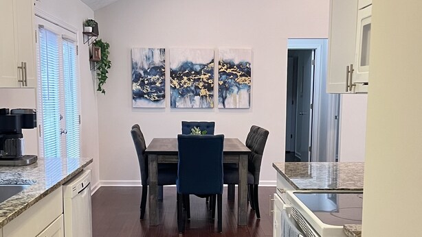 A modern kitchen with white cabinets, a dining area with a table and chairs, and a large window with blinds.