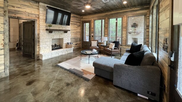 Amplia sala de estar con chimenea de piedra, televisor de pantalla plana grande montado encima y sofá seccional gris.