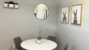 Un coin repas avec une table ronde, quatre chaises, une plante en pot et deux tableaux encadrés au mur.