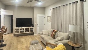 Un salon équipé d’un ventilateur de plafond, d’un téléviseur à écran plat, d’un canapé, d’une table basse et d’une lampe.