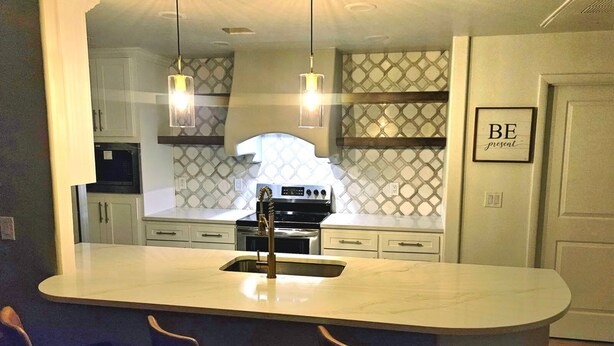 Une cuisine moderne dotée d’un îlot central, de luminaires suspendus et d’une cuisinière en acier inoxydable.