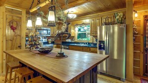 A wooden interior with a central island, bar stools, a refrigerator, and hanging lanterns.