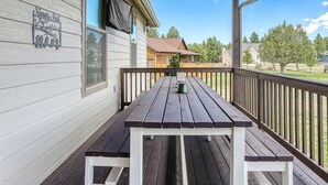 A covered patio with a wooden table and benches, a metal sign on the wall, and a view of a residential area with houses and trees.