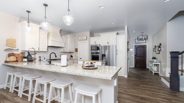 A modern kitchen with white cabinetry, a large island with bar stools, stainless steel appliances, and pendant lighting.