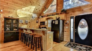 Une cuisine rustique, située dans une cabane en bois, avec un coin bar, des meubles de rangement en bois et un grand réfrigérateur noir.