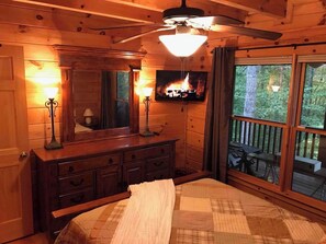 A cozy cabin bedroom with a bed, dresser, and a large window overlooking a deck.