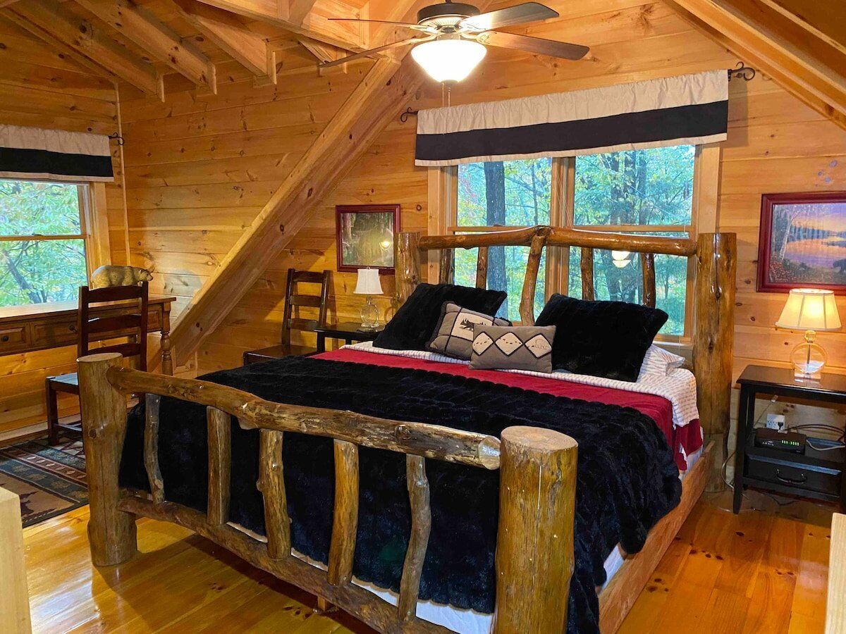 Een slaapkamer in een houten hutje, met een bed, een stoel, een nachtkastje en een raam.