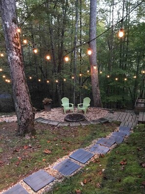 An outdoor seating area with two green chairs, a fire pit, and string lights.