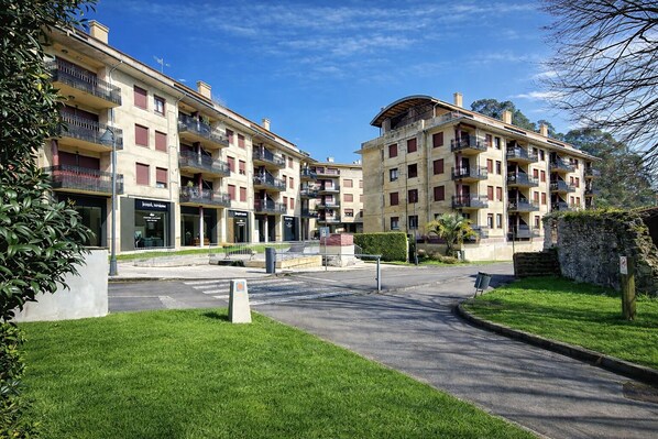 Un immeuble résidentiel doté de nombreux balcons, d’une entrée pavée et d’un petit jardin.
