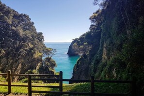 A coastal view with a wooden fence in the foreground, a narrow passage between cliffs, and a clear blue sea. - Apartamento Vacacional La Madora (Llanes)