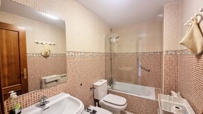 Une salle de bain équipée d’un lavabo, de toilettes et d’une baignoire, avec des carreaux décoratifs et une porte en bois.