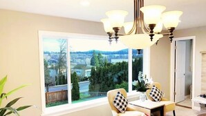 Un salon moderne doté d’une grande fenêtre, d’un lustre et offrant une vue sur un quartier résidentiel.