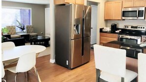 Une cuisine moderne dotée d’appareils électroménagers en acier inoxydable, de meubles en bois et d’un coin repas avec des chaises blanches.