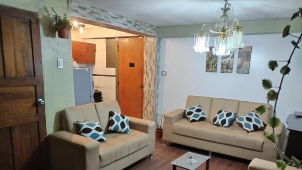 A living room with two sofas, a coffee table, and a wooden floor. There is a door leading to a kitchen and a hallway. - Casa de Fabrizio en Cusco, Ideal Para Familias (Cusco)