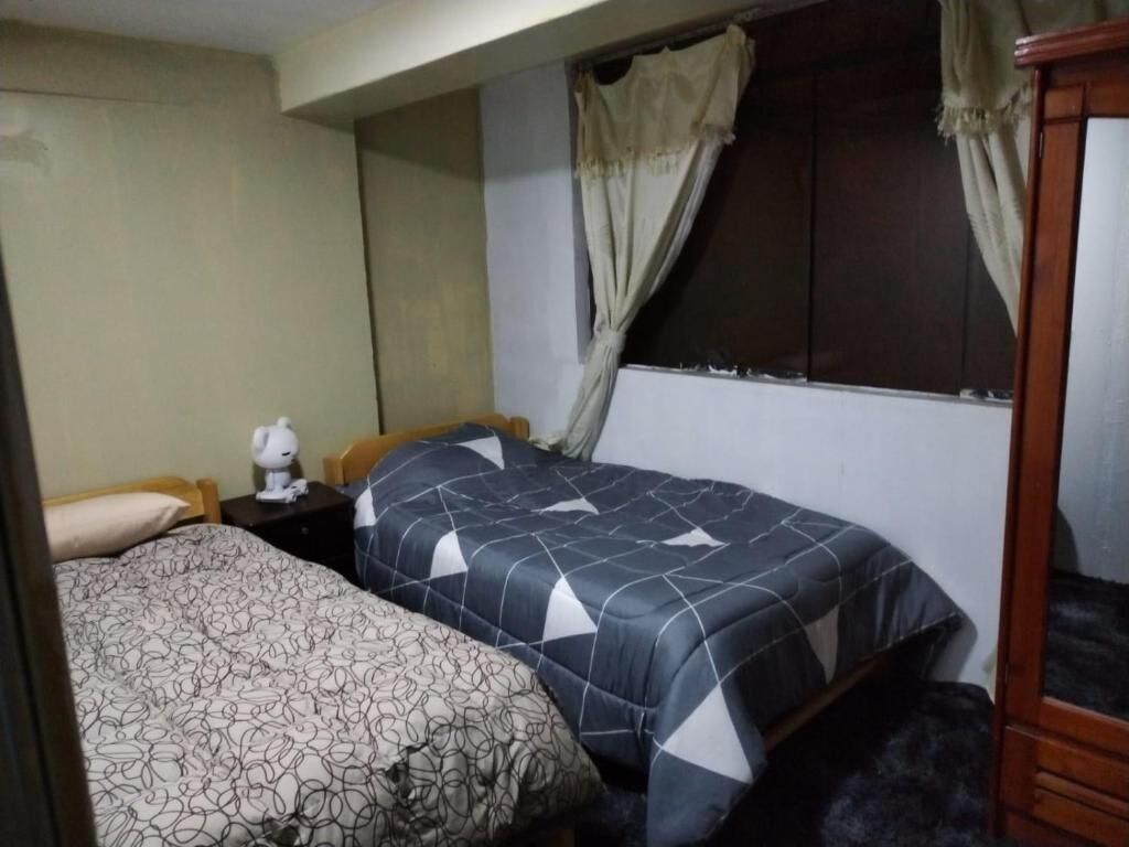 A bedroom with two beds, a nightstand with a lamp, and a window with curtains.
