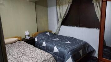 A bedroom with two beds, a nightstand with a lamp, and a window with curtains.