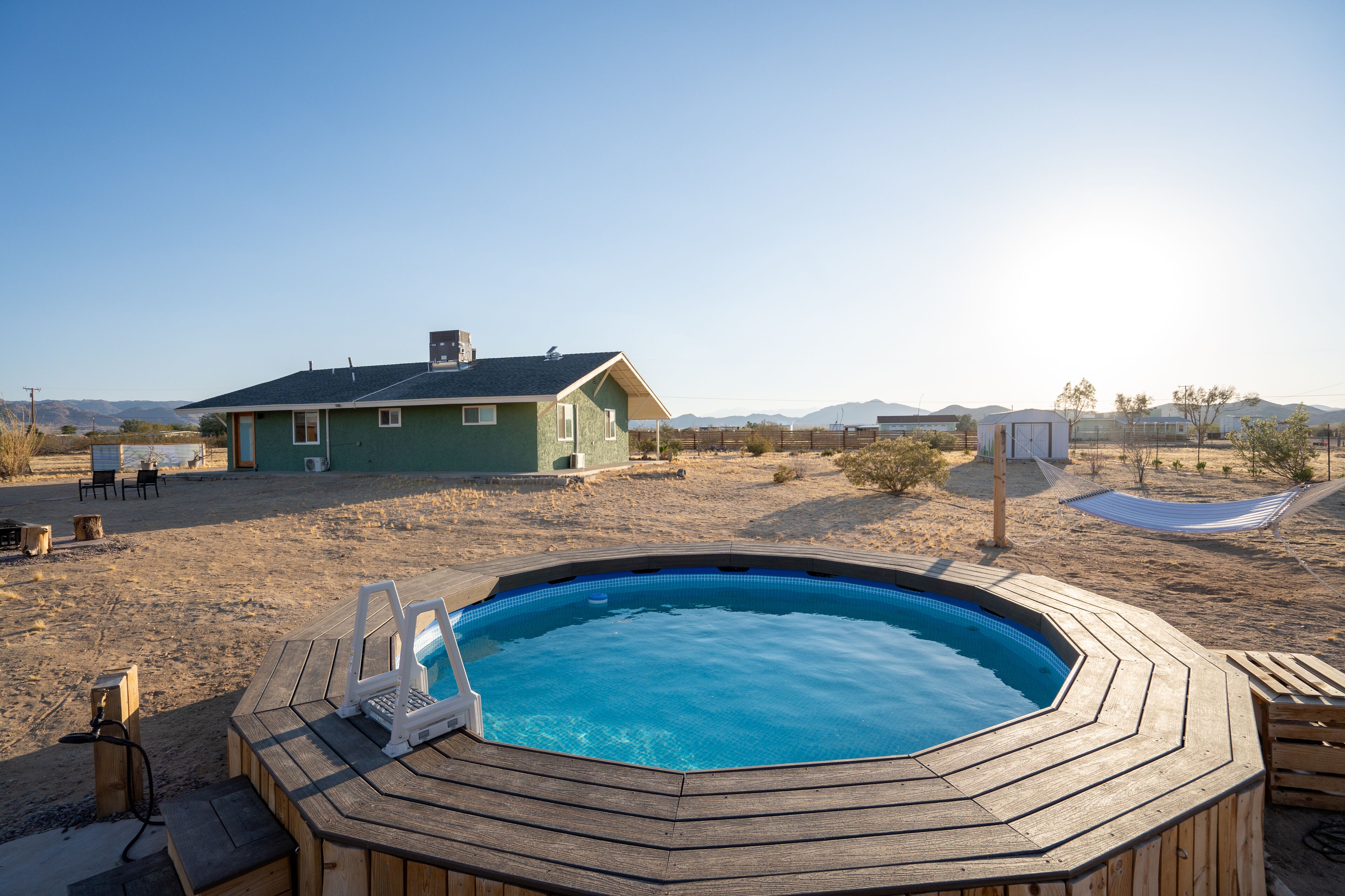 A wooden hot tub with a laptop, a house in the background, and a clear sky.