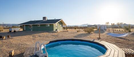 A wooden hot tub with a laptop, a house in the background, and a clear sky.