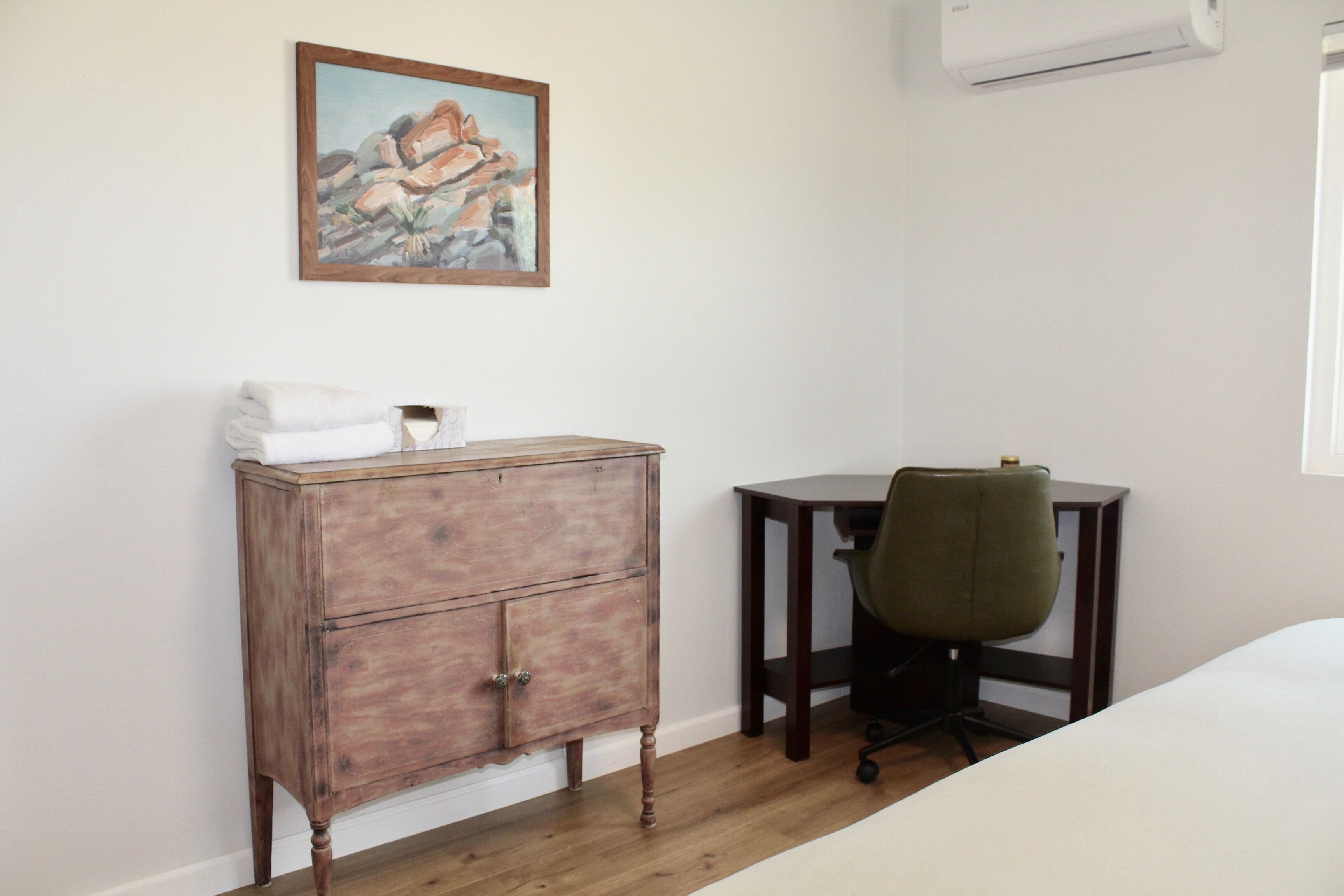 A room with a wooden dresser, a desk with a chair, and a bed.