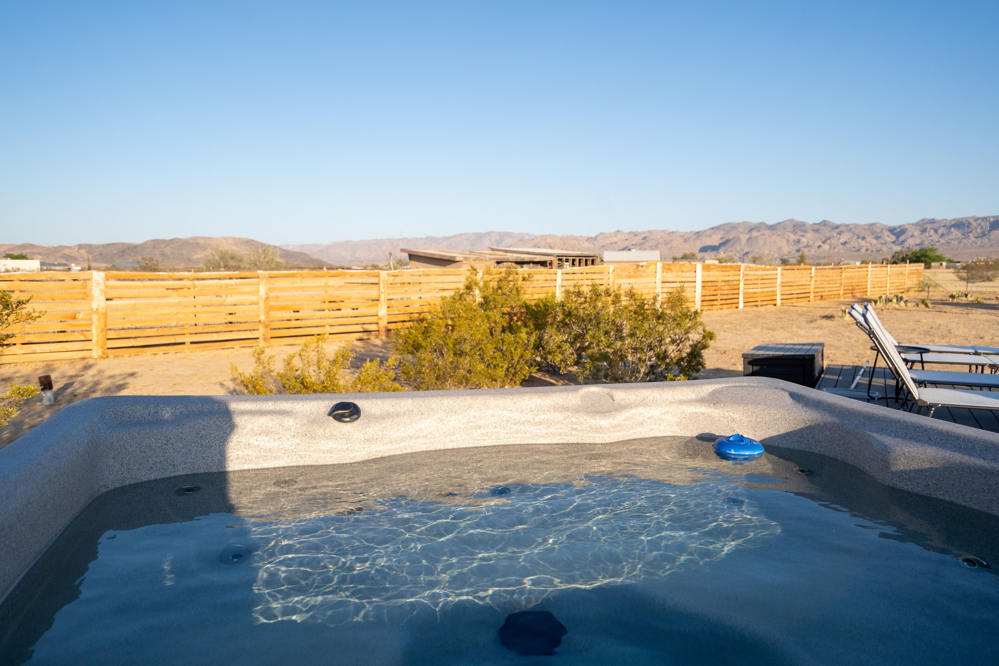 A hot tub with a wooden fence and mountains in the background.