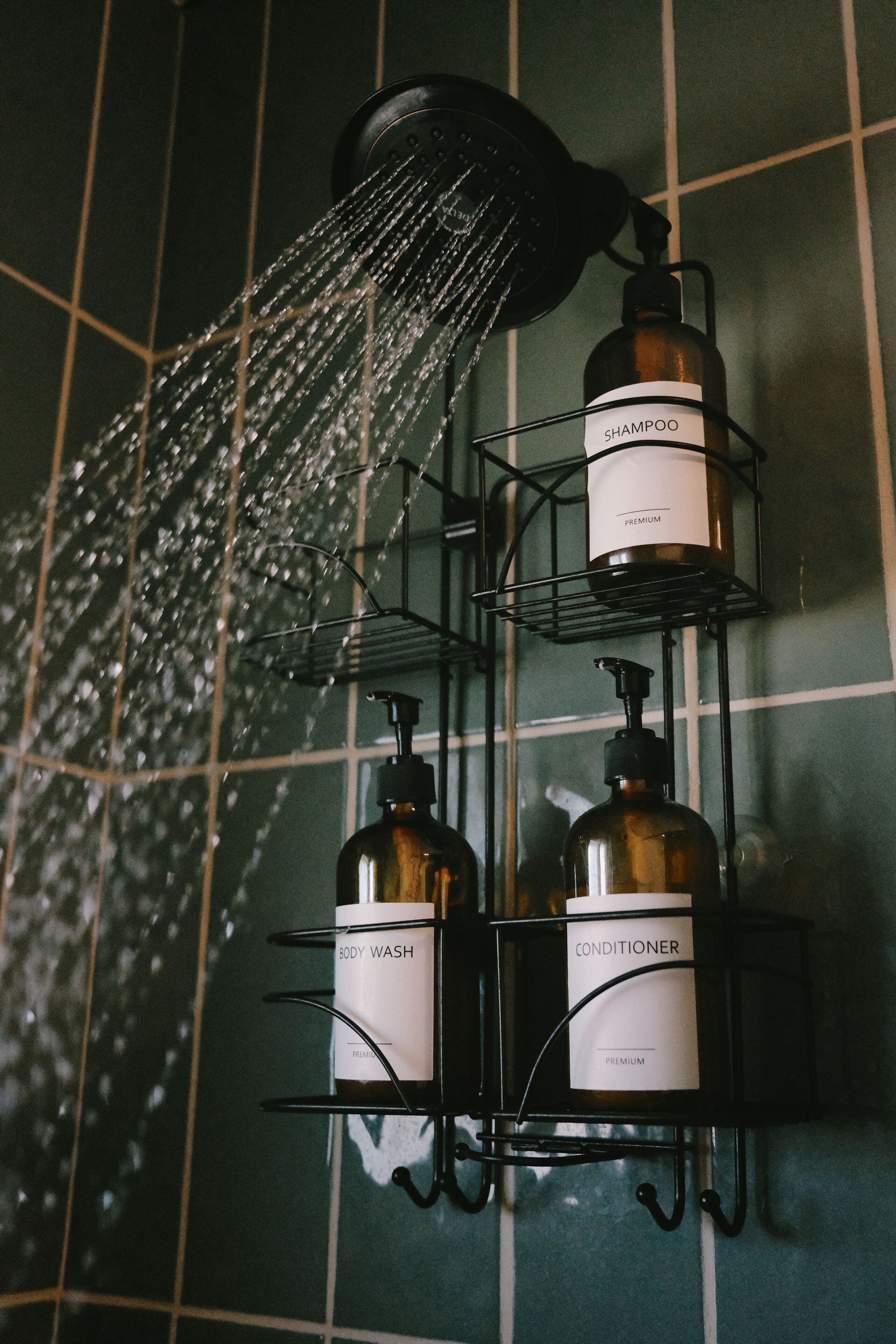 Un baño con cabezal de ducha, un estante en la pared que contiene botellas de champú y acondicionador, y una botella de gel de baño.