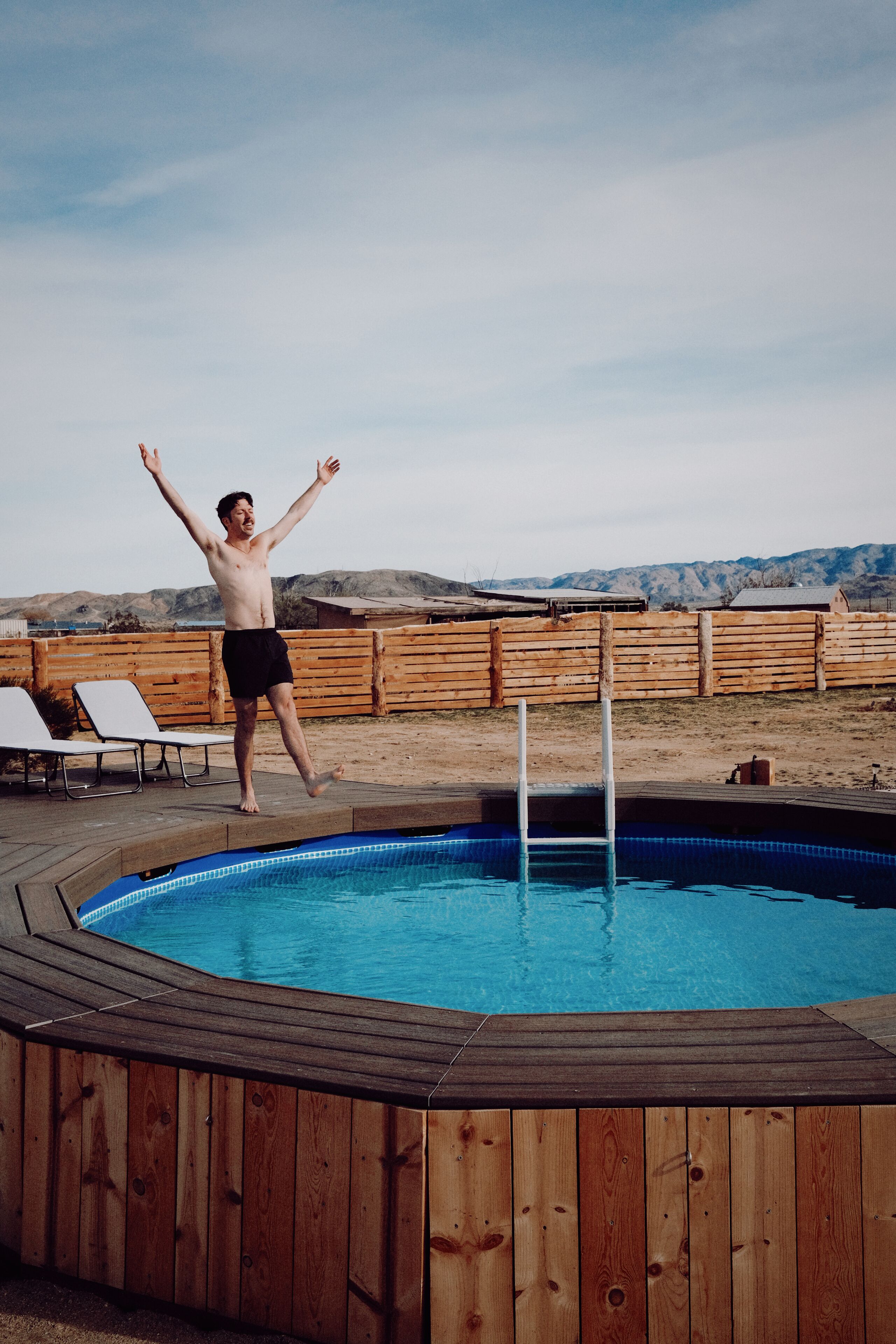 Une terrasse en bois avec une piscine, une clôture en bois et une chaise au fond.