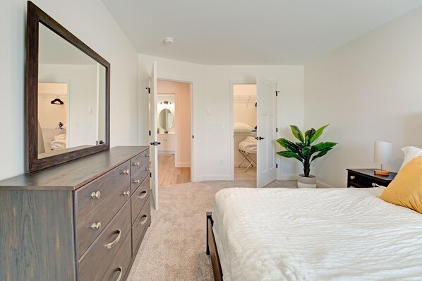 A bedroom with a large mirror, a bed, a dresser, and a potted plant.