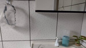 Ein Badezimmer mit einem weißen Waschbecken, einem weißen Handtuchhalter, einem blauen Zahnbürstenhalter und einer kleinen Topfpflanze.