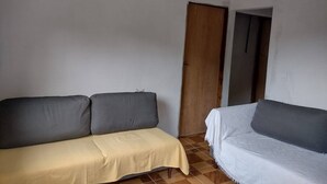 Ein Zimmer mit einer Couch, einem Bett, einer Holztür und einem Fliesenboden.