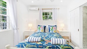 A bedroom with a bed, two bedside tables, an air conditioning unit, and a window with curtains. - Moonflower Villa: Luxe Oasis in Sunset Crest, Holetown (Sunset Crest)
