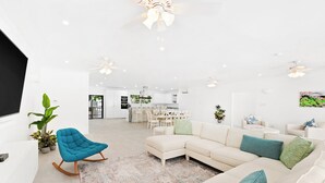 Un salon moderne avec un canapé d’angle, un fauteuil à bascule et un coin repas à l’arrière-plan.