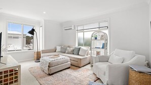 A modern living room with a beige sofa, a white armchair, and a patterned rug. - Jan Juc Surfview Beach House Beach, Golf & Cafes (Jan Juc)