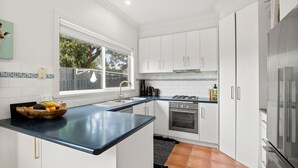 A modern kitchen with white cabinets, a black countertop, a gas stove, and a refrigerator. - Jan Juc Surfview Beach House Beach, Golf & Cafes (Jan Juc)