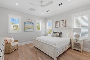 A bedroom with a bed, a nightstand, a wicker chair, and artwork on the walls.