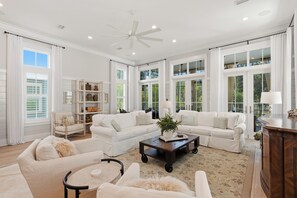 A spacious living room with white furniture, large windows, and a ceiling fan.