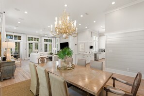 A spacious dining area with a large wooden table, multiple chairs, a chandelier, and a view of the kitchen and living room.