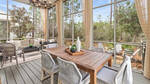 Eine überdachte Terrasse mit einem Holztisch, Korbstühlen und einem Deckenventilator.
