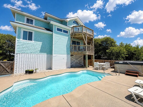 A two-story house with a swimming pool, outdoor furniture, and a wooden deck.