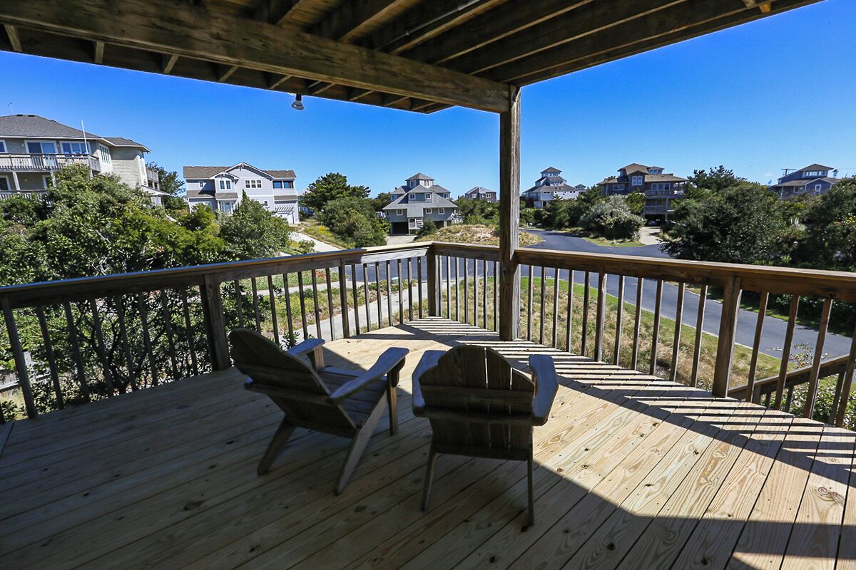 A wooden deck with two Adirondack chairs, overlooking a residential area with houses and trees.