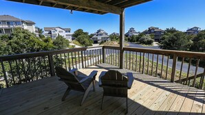 Un terrazzo in legno con due poltrone Adirondack, con vista su una zona residenziale con case e alberi.