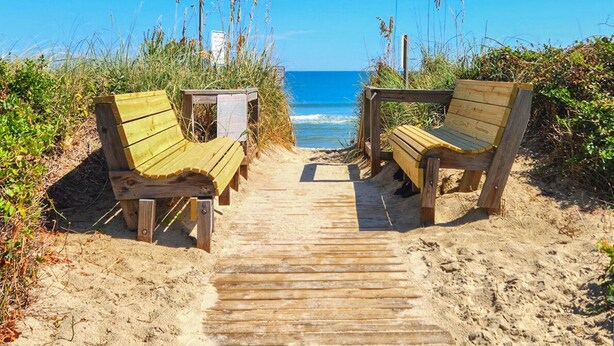 Un sentiero di legno conduce a sdraio su una spiaggia sabbiosa, con l'oceano sullo sfondo.