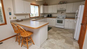 Una cucina con isola centrale, sedie in legno, mobili bianchi, un piano cottura e un frigorifero.