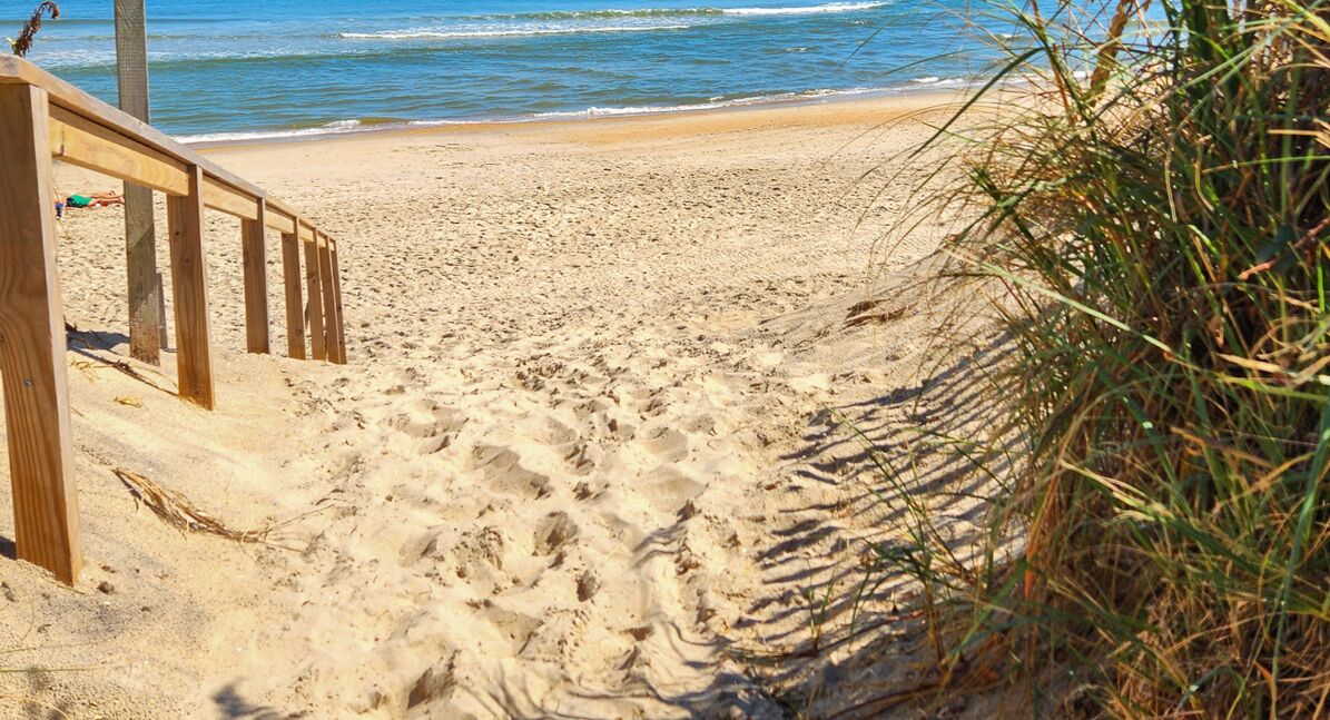 A sandy beach with a wooden walkway leading to the water.