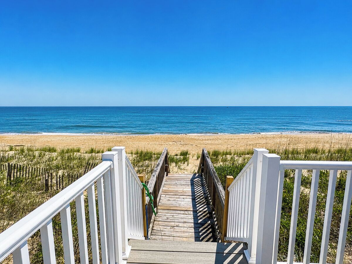 A wooden boardwalk leading to a beach with a clear blue sky.