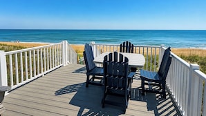 Une terrasse en bois avec une table et des chaises, donnant sur une plage.